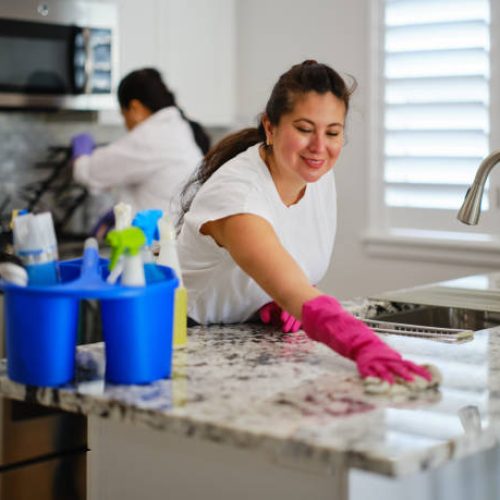 Two women in a home cleaning a kitchen.
